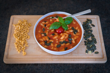 ready to eat - homemade hot tomato soup in a white bowl with basil, cherry tomatoes, creamy, croutons, noodles and roasted pumpkin seeds