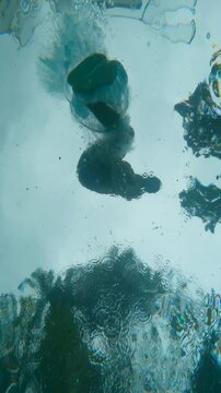 Experience the world beneath the rain-soaked surface. Crystal-clear waters reveal a young man doing a sideflip, captured in slow motion. Dark, cloudy skies frame the scene, surrounded by lush trees. 