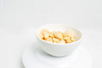 Peeled garlic cloves in a white plate on a white background.