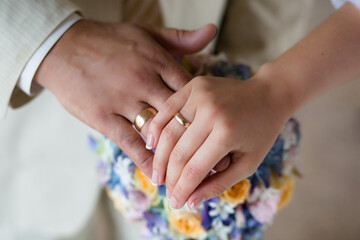 Close-up of newlyweds' hands, with an emphasis on wedding rings, against a background of a flowers.