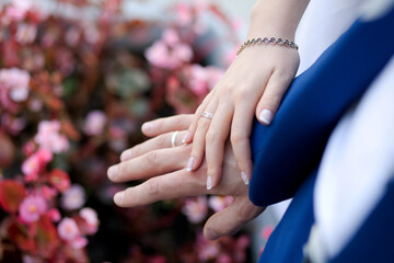 Close-up of Hands with Wedding Rings and Bracelet Against Floral Background