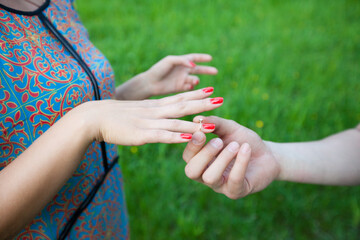 Close-up of Hands with Red Nails Exchanging Ring on Green Background