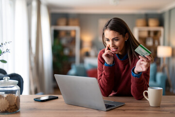 Shopaholic businesswoman with credit card buying online over laptop while sitting at desk at home. - obrazy, fototapety, plakaty
