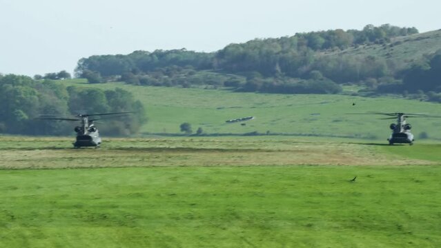 a pair of RAF Chinook tandem-rotor CH-47 helicopters descend and land in a grass field