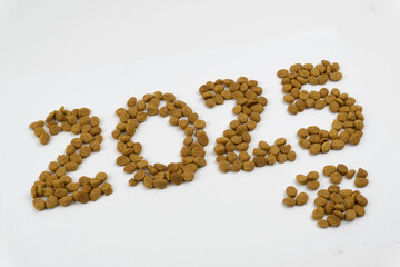 Year 2025 and cute paw written with granule dog food. Diagonal.
