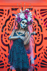Mexican woman dressed and characterized as a catrina for the Day of the Dead festivity, behind her an orange background like the cempasuchil flower.