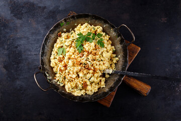 Traditionelle Allgäuer Käsespätzle mit Walnüssen serviert als Draufsicht in einer Eisenpfanne auf einem rustikalen Holzbrett auf einer Berghütte