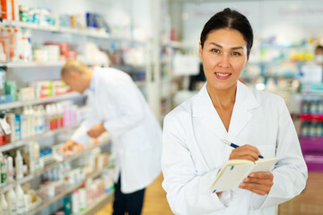 Portrait of an female pharmacist working in pharmacy during the pandemic, standing in trading floor and makes important notes