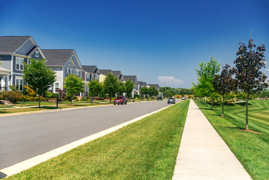 Quiet street in a residential area in the suburbs. Rows of houses along the sidewalk with a green lawn.