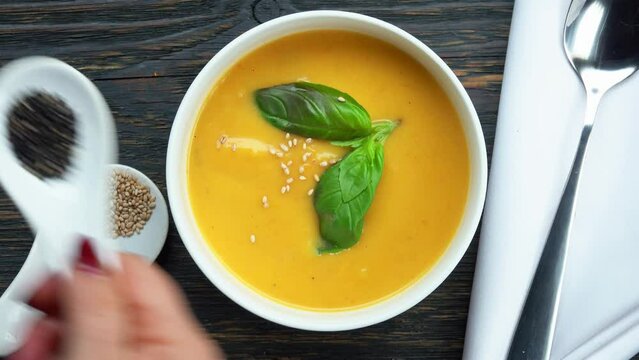 hand sprinkles white black sesame seeds on pumpkin soup