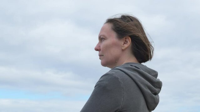 Side view of serious adult female brunette in her 40s standing outdoors and thinking