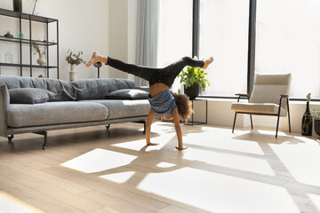 Talented gymnast kid doing upsidedown acrobatic handstand with splits in air, exercising on floor in living room. African American kid training body, sportive skills at home. Childhood, sport concept - Powered by Adobe