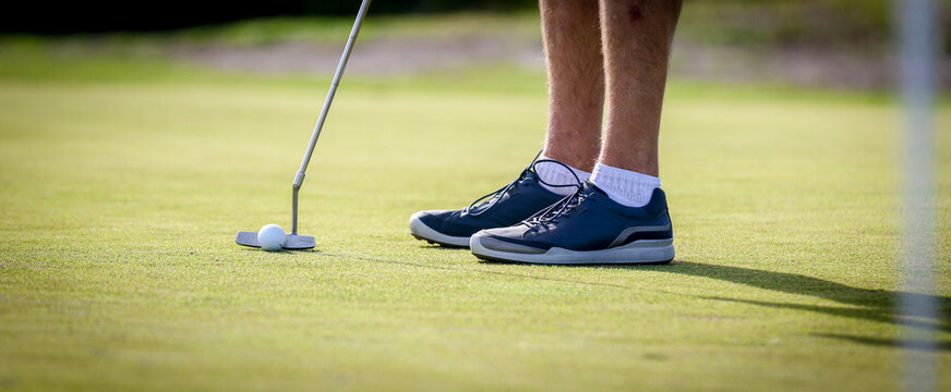 Man in blue shoes lining up his golf shot holding a putter on a golf course in Central Florida