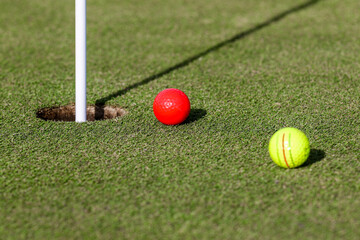 Red golf ball next yellow golf ball close to putting green hole waiting to be tapped in at a golf course in Central Florida