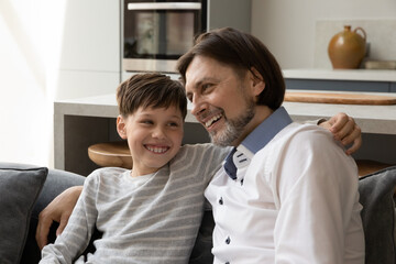 Happy 40s dad and teen son with teeth braces enjoying close friendship, spending leisure time at home together, chatting, laughing, talking with trust. Cheerful father embracing kid, giving support