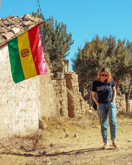 mulher caminhando ao lado de casas de adobe com bandeira da bolivia hasteada 