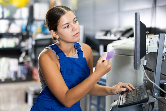 Warehouse girl employee looks at computer monitor screen and checks completeness of order for customer. Female worker of paint shop reads customers input data on computer