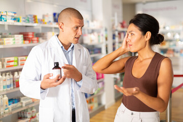 Asian woman complaining about headache to pharmacist in drugstore and he proposing treatment to her.