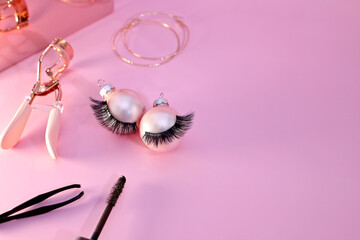 False eye lashes and curler tool with Christmas decoration, pink background, copy space