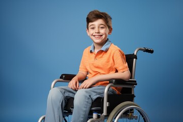 Obraz premium Joyful young boy wearing a bright orange polo shirt, seated confidently in a wheelchair against a deep blue background