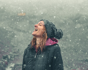 mulher com touca de lã e mãos levantadas, sorrindo, em cenário de inverno com neve caindo 