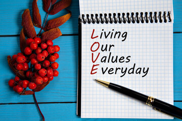 LIVING OUR VALUES EVERYDAY - words in a white notebook on a wooden blue background with a rowan...