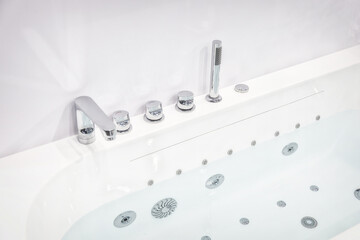 White acrylic bathtub with modern faucets and shower. The taps and mixer are made in chrome design....