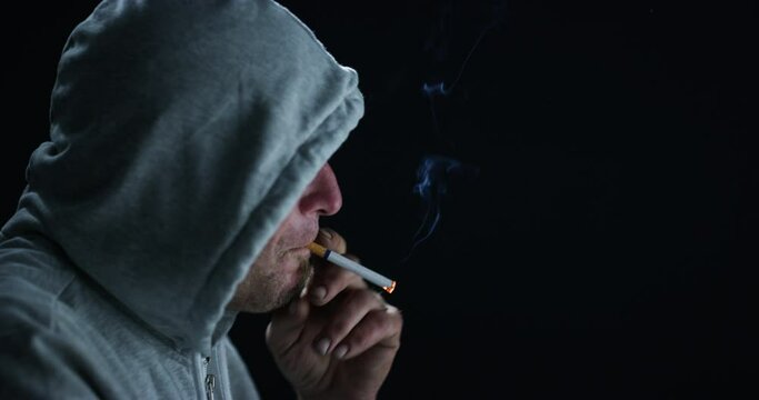 Man, smoking cigarette and lighter by dark background in profile for thinking, stress or bad habit in hoodie. Guy, addiction and mental health with tobacco product for anxiety, idea or flame in night