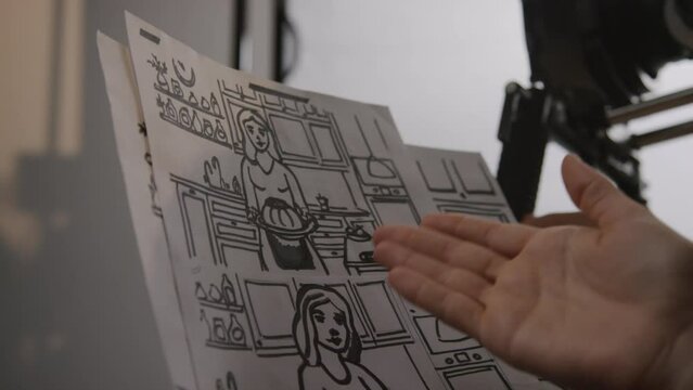 Close-up shot of hands of unrecognizable female director and cameraman planning upcoming commercial shoot in studio, pointing at scenes in storyboard and discussing frame composition