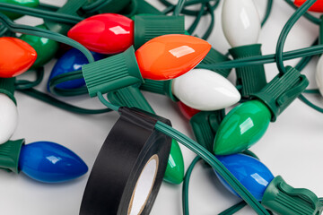 Repairing wires on Christmas string lights with electrical tape. Holiday lighting repair, safety and decoration concept.