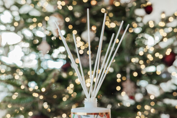  Christmas Scent . Diffuser with sticks with aroma of vanilla, oranges and cinnamon on Christmas shining tree bokeh background.Fragrance diffusers for home 