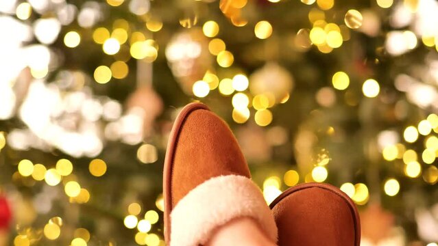 Christmas cozy mood. legs in fur slippers on a Christmas tree in garlands background. Winter holidays and recreation. High quality 4k footage