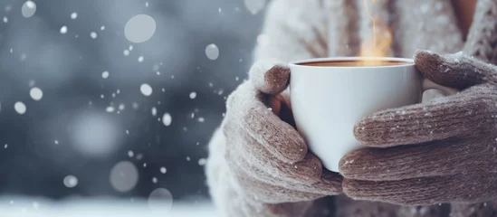 Fototapeten Winter concept Womens mittened hands hold a warm beverage outdoors © AkuAku
