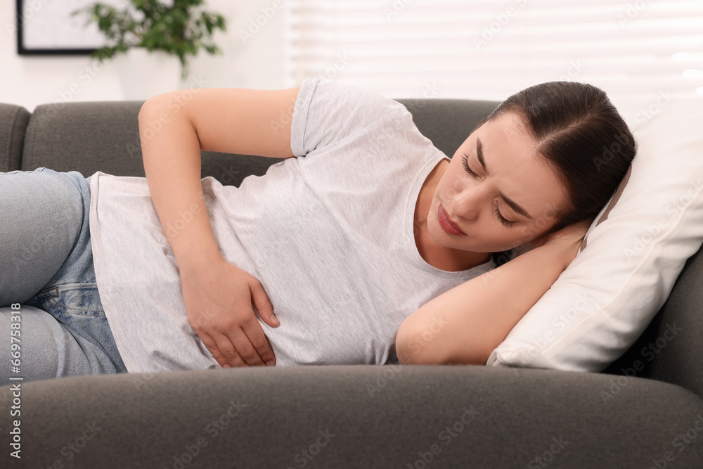 Canvas Prints Woman suffering from abdominal pain while lying on sofa at home. Unhealthy stomach