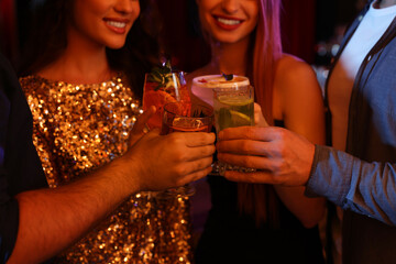 Friends clinking glasses with fresh cocktails in bar, closeup