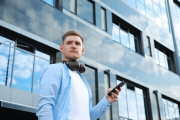 Man with headphones and smartphone near building outdoors, low angle view. Space for text