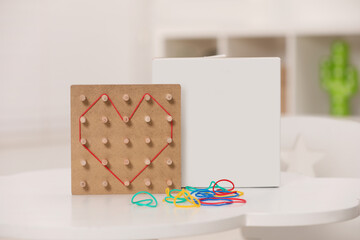 Wooden geoboard with rubber bands on white table indoors. Educational toy for motor skills development