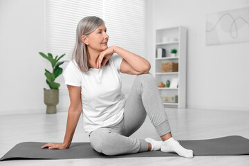 Senior woman sitting on mat at home. Yoga practice