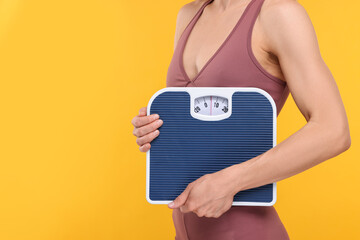 Slim woman holding scales on yellow background, closeup and space for text. Weight loss
