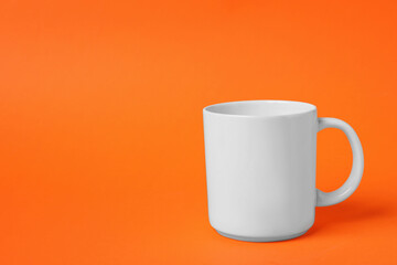 One white ceramic mug on orange background, space for text
