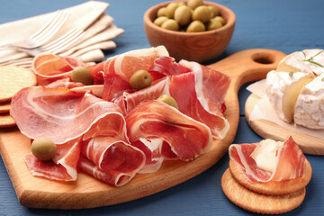 Slices of tasty cured ham, olives and cheese on blue wooden table, closeup