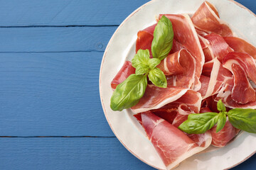 Slices of tasty cured ham and basil on blue wooden table, top view. Space for text