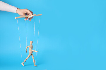 Woman pulling strings of puppet on light blue background, closeup