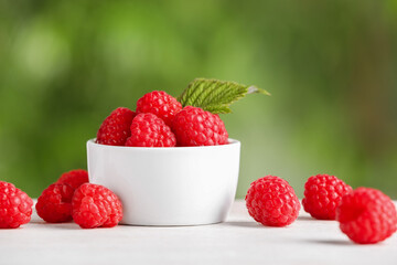 Tasty ripe raspberries and green leaf on white table outdoors