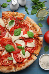 Delicious Caprese pizza and ingredients on blue wooden table, flat lay