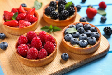 Tartlets with different fresh berries on light blue table, closeup. Delicious dessert