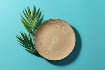 Ceramic plate and green leaves on turquoise background, flat lay