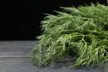 Fresh green dill on grey wooden table against black background, closeup. Space for text