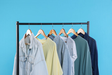 Rack with stylish clothes on wooden hangers against light blue background