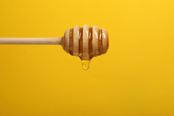 Pouring honey from dipper against yellow background, closeup. Space for text